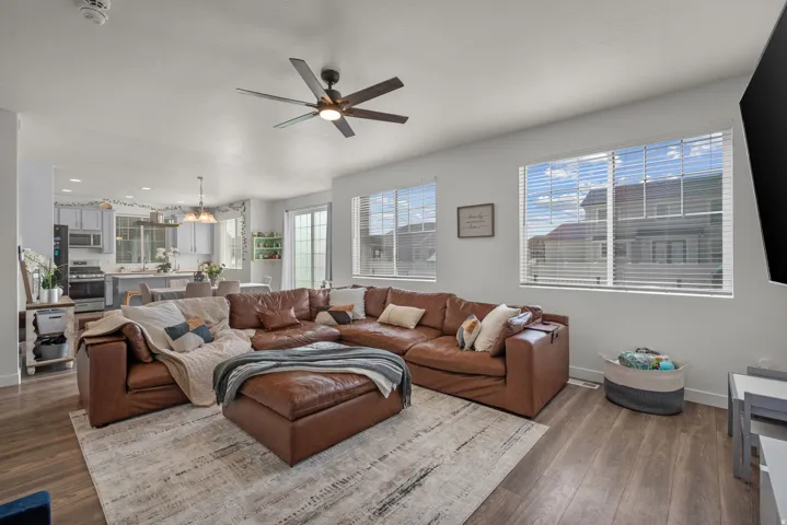 Open-concept living space featuring wood-finish flooring, a ceiling fan, and multiple windows