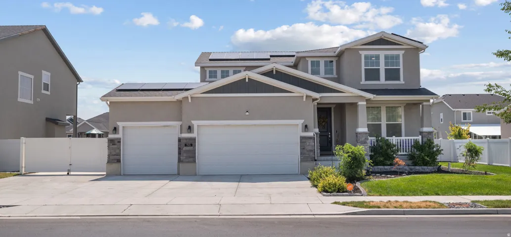 Stucco and stone facade with a covered porch, two-car garage, and solar panels