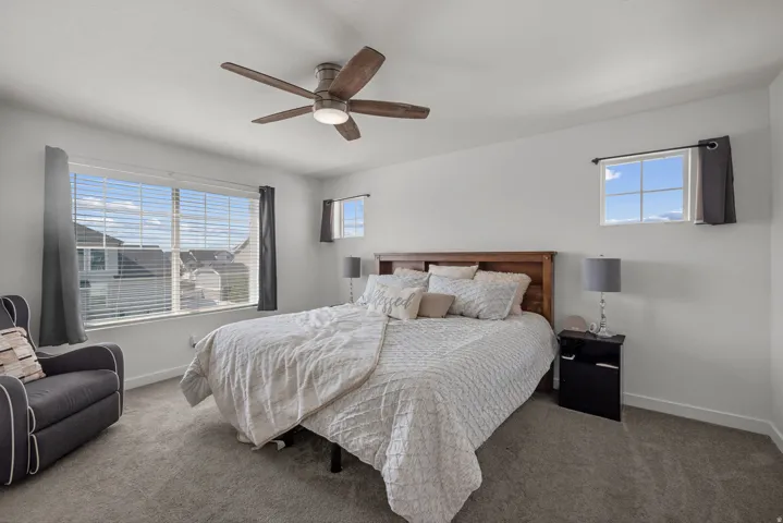 Wood-finish ceiling fan with integrated lighting, large windows with blinds, plush carpeting, and built-in headboard