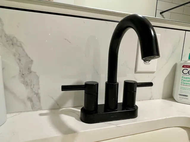 Matte black faucet with dual lever handles, set against a white countertop and marble-patterned wall tile