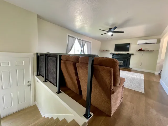 Wood-finish flooring, black railing, white interior door, ceiling fan, and a fireplace with a mantel