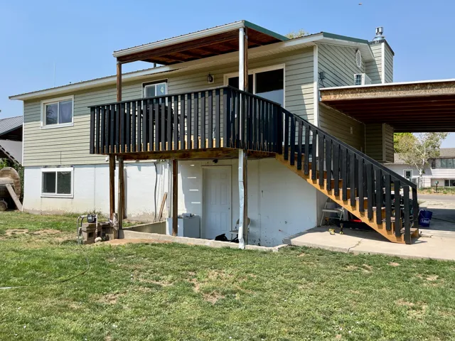 Exterior featuring light green horizontal siding, a full-length deck with dark railings, exterior stairs, and a covered carport