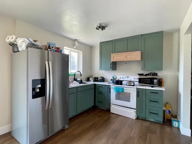 Kitchen featuring wood-finish flooring, green shaker-style cabinetry, light countertops, and a stainless steel refrigerator
