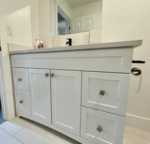 White vanity with shaker-style cabinetry, square pulls, and a light-toned countertop