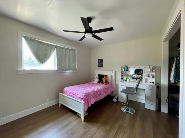 Wood-finish flooring with a neutral wall color, overhead ceiling fan, and a single window with white trim