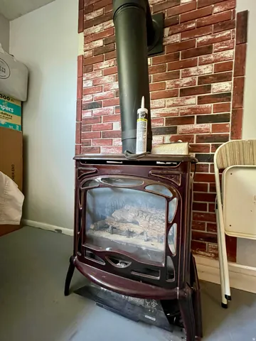 Freestanding stove with a metal flue, set against a brick-finish wall