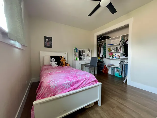 Recessed window with white trim, wood-finish flooring, ceiling fan with black blades, and an open closet with built-in shelving and hanging rods