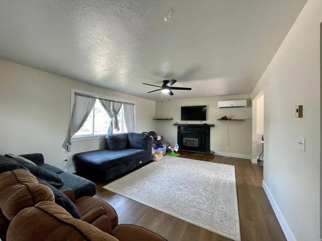 Living space featuring wood-finish flooring, a ceiling fan, a fireplace with a dark surround, and a window with white trim