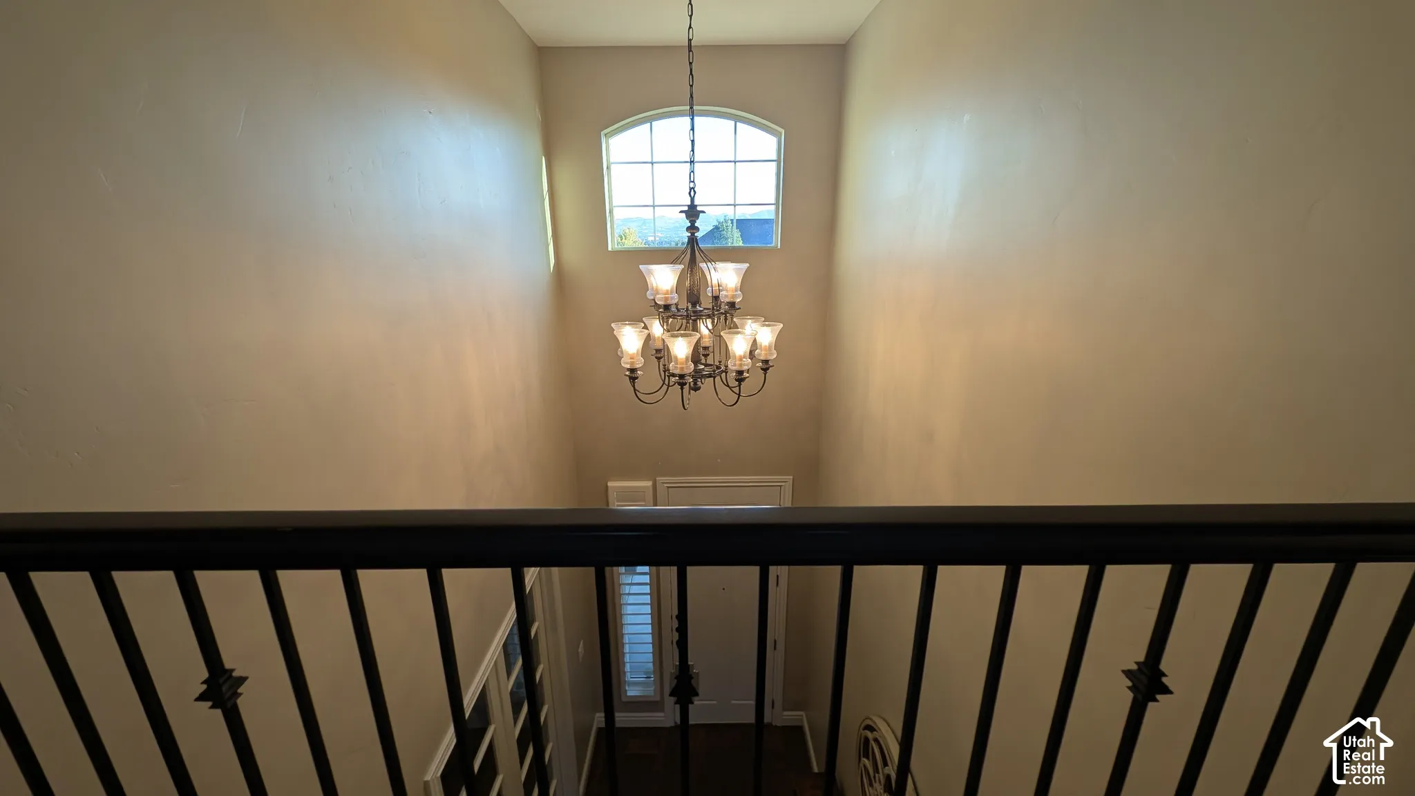 Two-story entryway with arched window, wrought iron railing, and suspended chandelier