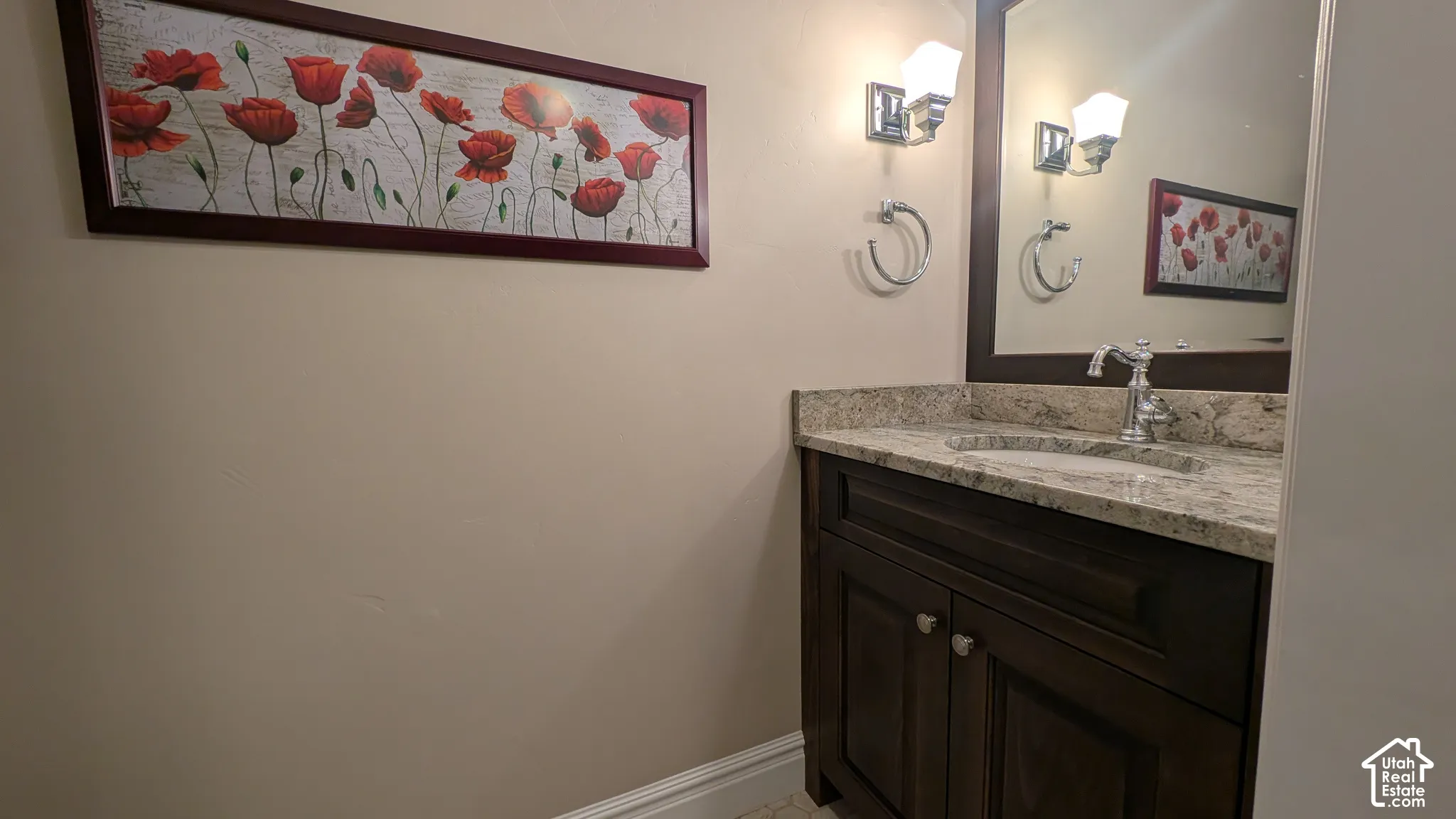 Built-in vanity with a stone countertop, undermount sink, wall-mounted mirror, and sconce lighting