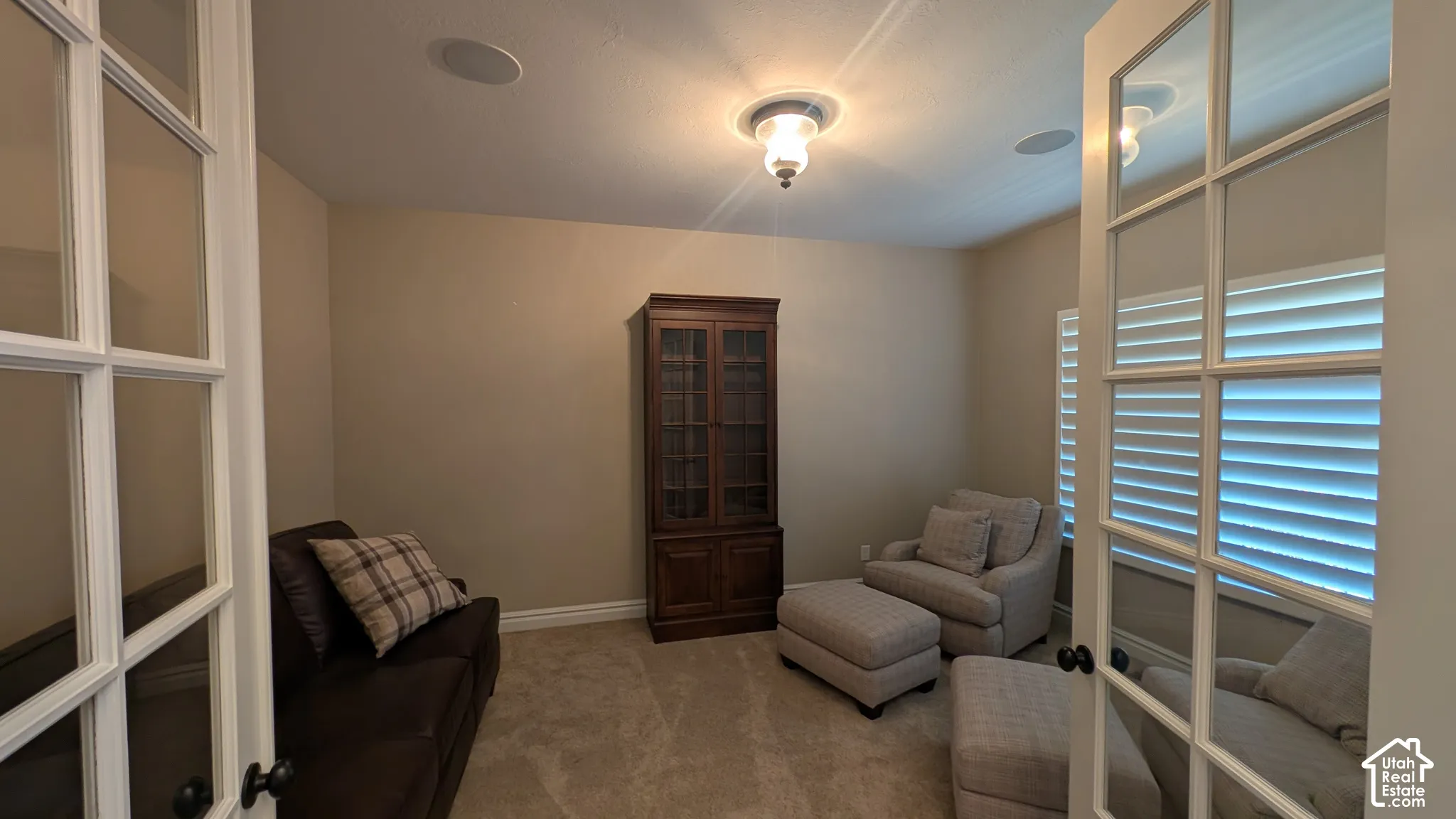 Glass-paneled double doors open to a room featuring ceiling-mounted speakers, a flush-mount light fixture, and window plantation shutters