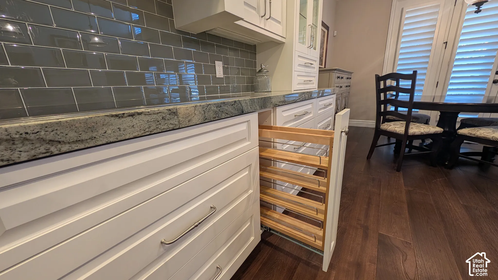 Built-in pull-out spice rack, white cabinetry with chrome hardware, speckled countertop, subway tile backsplash, and wood-finish flooring