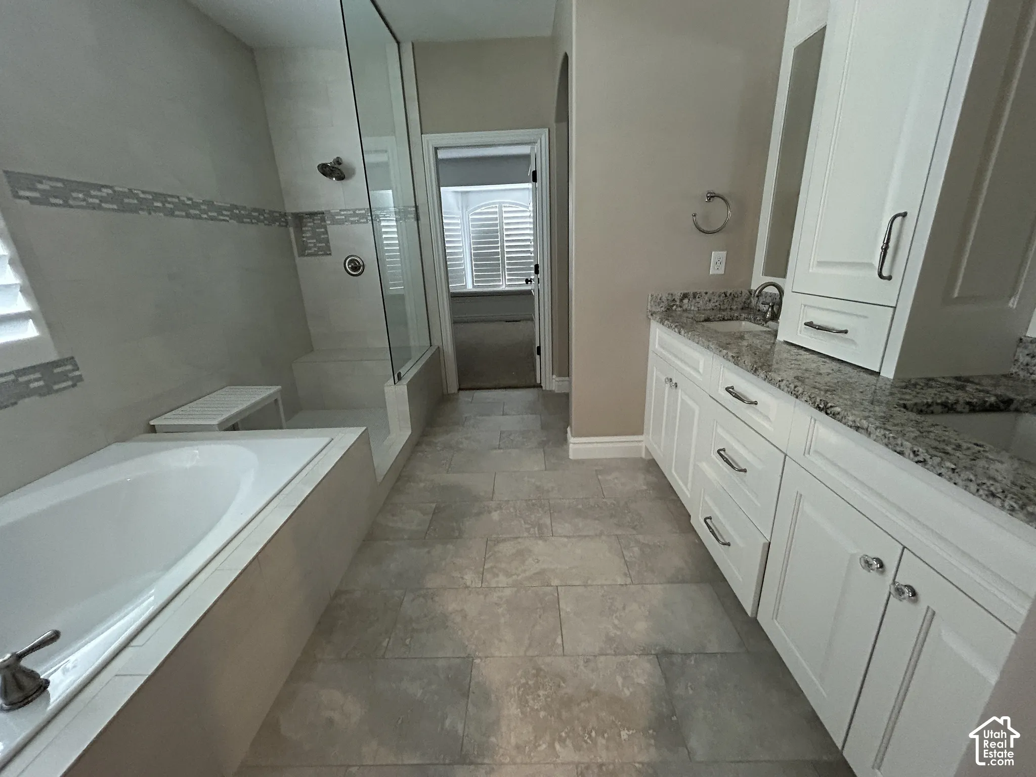 White built-in cabinetry with silver hardware, dual vanity with undermount sinks and stone countertops, tile flooring, and a walk-in shower with glass enclosure