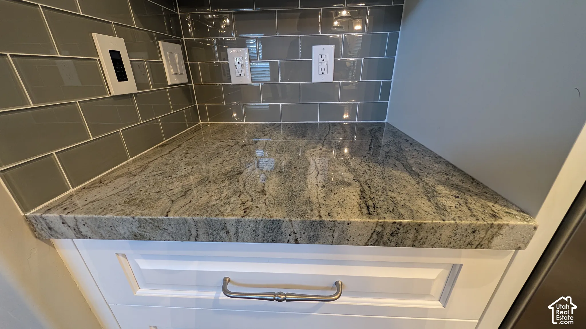 White cabinetry with brushed nickel hardware, natural stone countertop, and gray subway tile backsplash