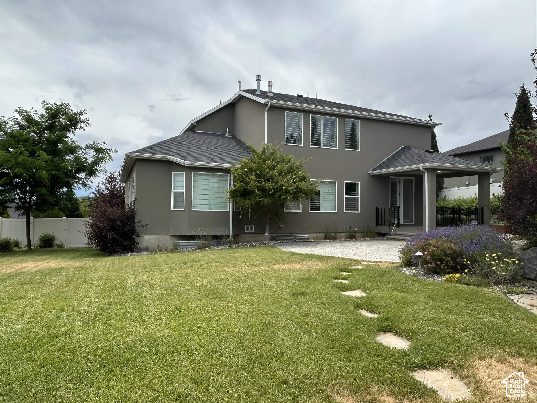 back side of home featuring Stucco exterior with multiple windows, covered patio, stone stepping path, and manicured lawn