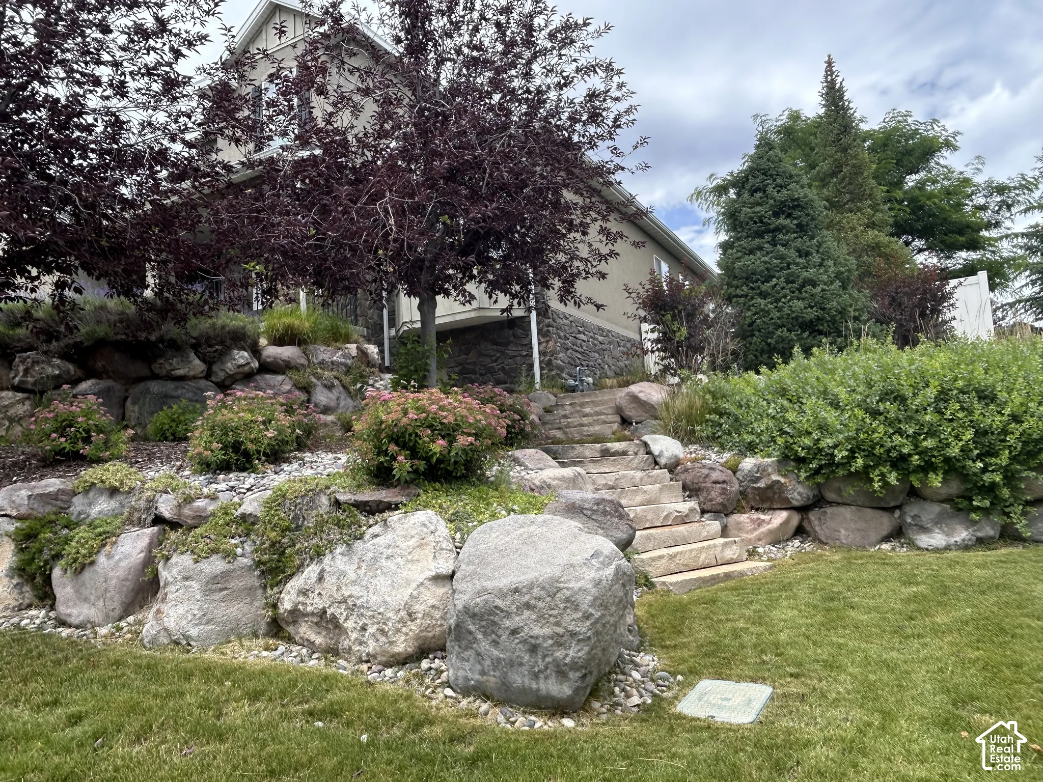 Manicured lawn with a terraced stone retaining wall, mature trees, and a stone staircase