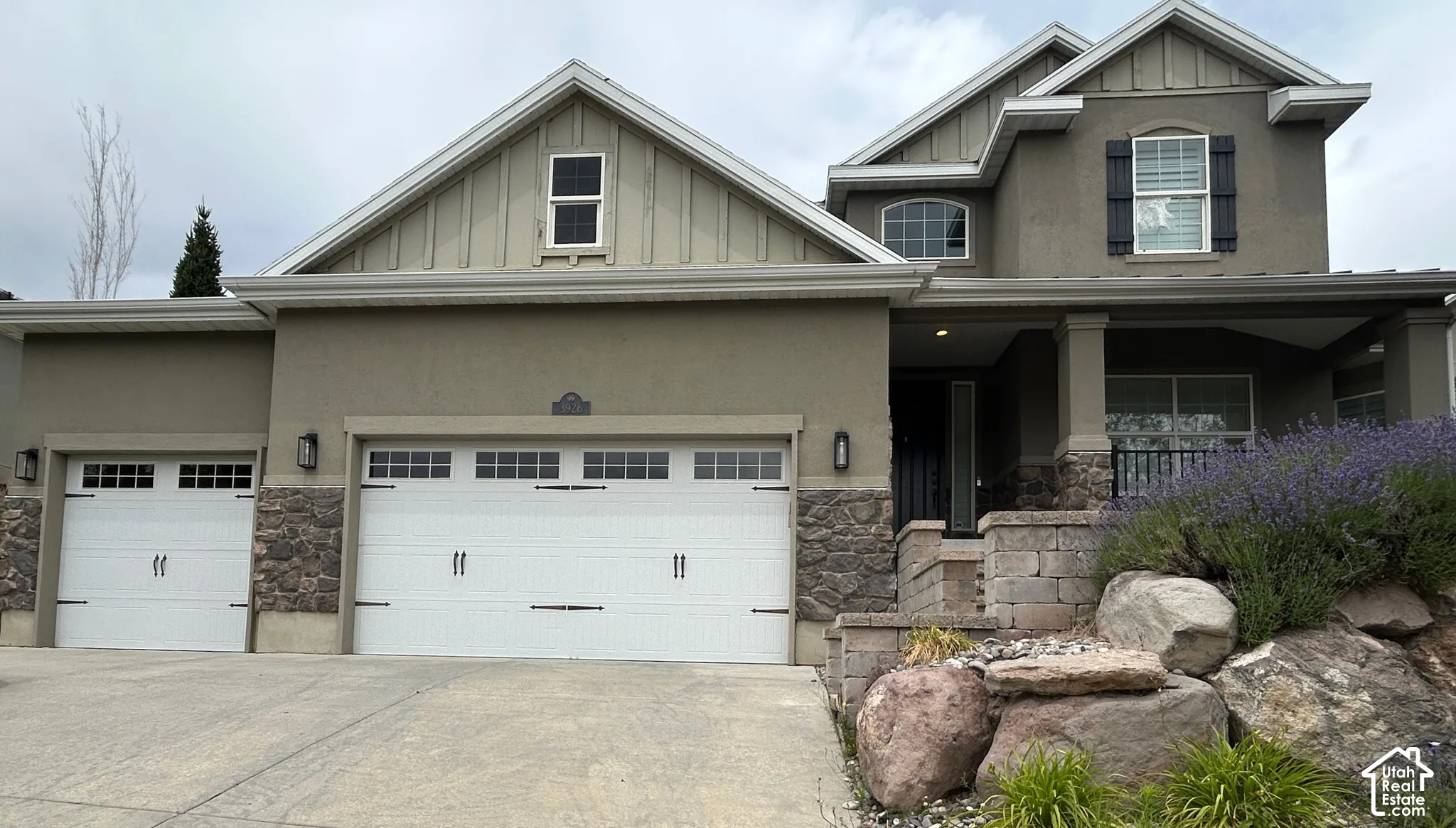 Stucco exterior with stone accents, covered front porch, and multi-pane garage doors