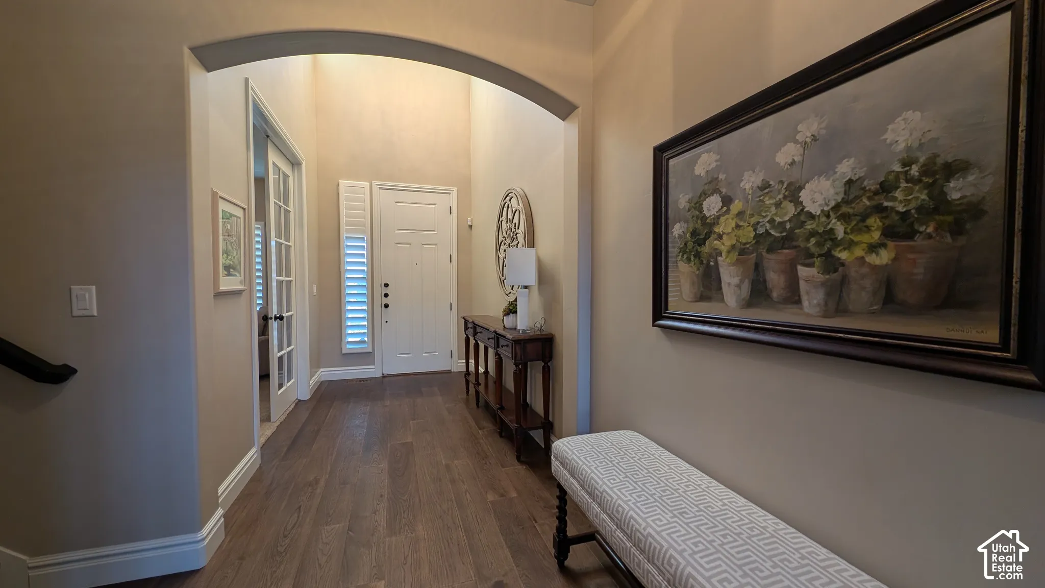 Arched entryway featuring wood-finish flooring, a paneled entry door, and side-light windows with plantation shutters