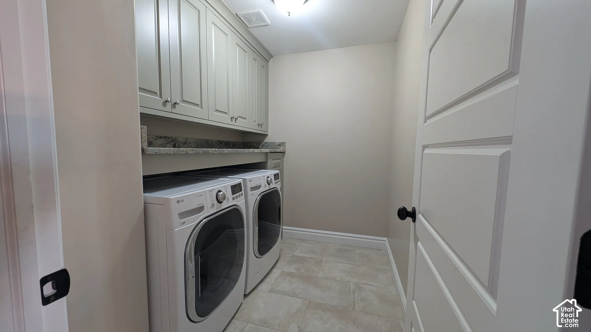 Functional laundry area featuring shaker-style cabinetry, a granite-finish countertop, and tile flooring