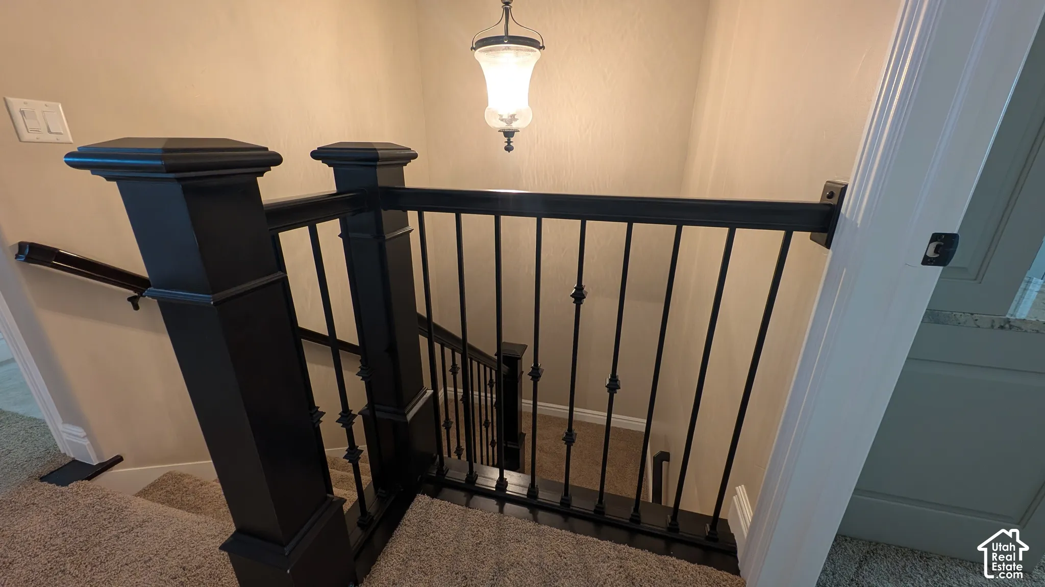 Staircase featuring dark wood newel posts, wrought iron balusters, and a clear glass pendant light fixture