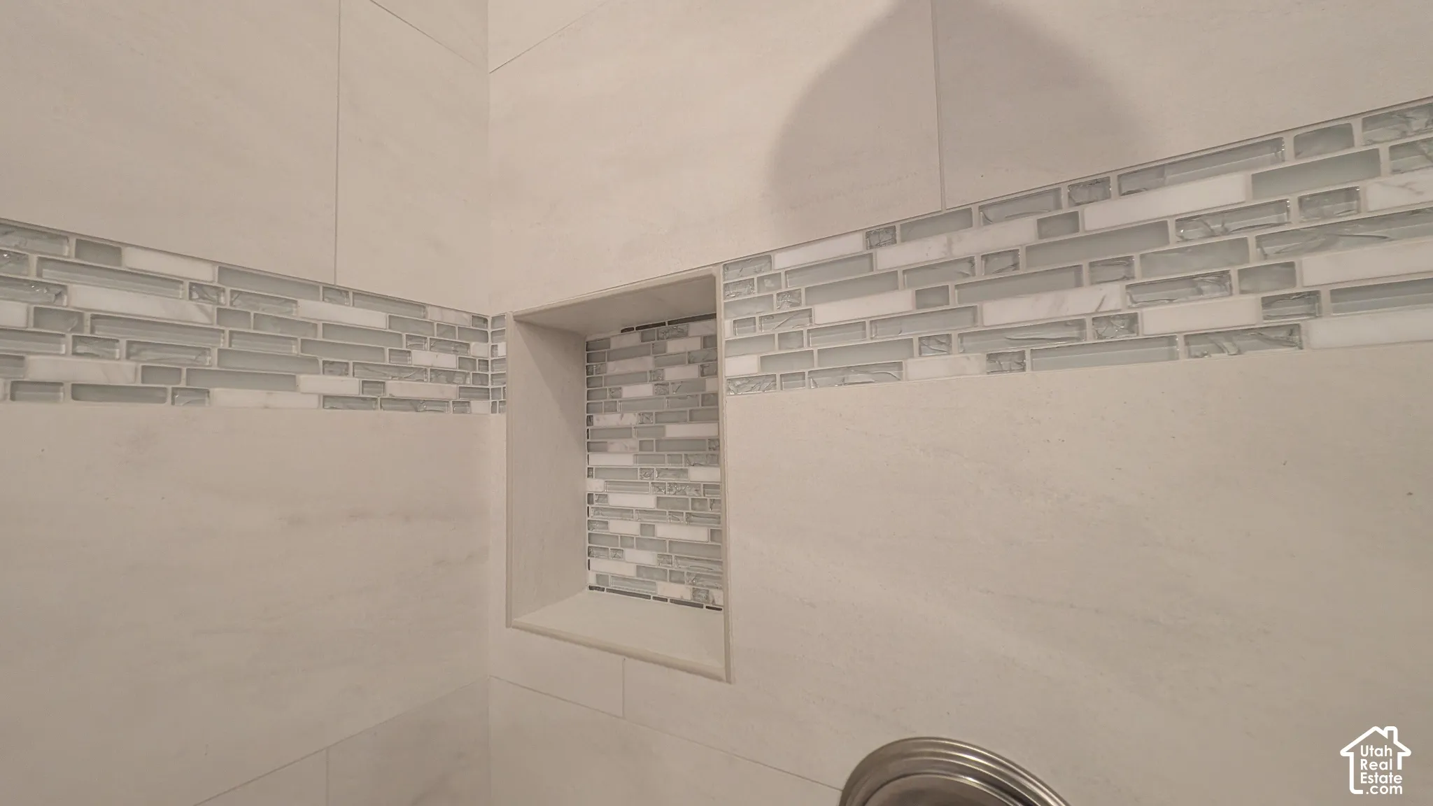 Tiled shower enclosure featuring light-toned large format tiles, a decorative glass and stone mosaic accent band, and a recessed niche with mosaic tiling