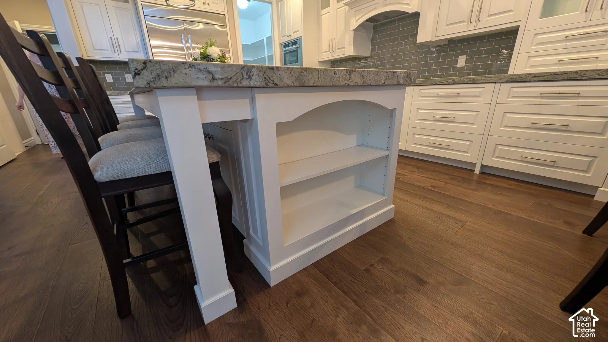 Kitchen island featuring a light-toned countertop, integrated shelving, and white cabinetry