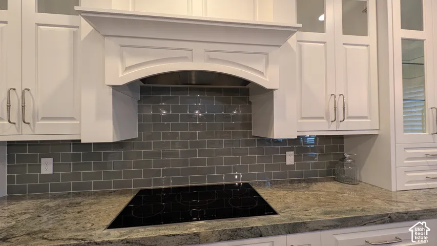 White cabinetry, stone-look countertops, glass-tile backsplash, and built-in cooktop