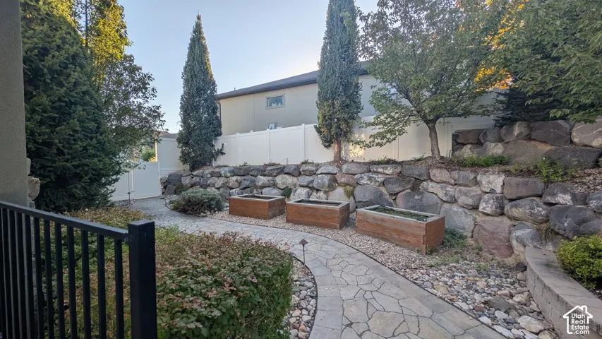 Stone paver pathway bordered by established landscaping, featuring three wooden planter boxes and a rock retaining wall
