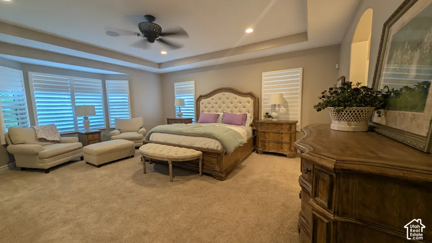 Master bedroom.  Furniture available for sale. Tray ceiling with recessed lighting, bay window with plantation shutters, ceiling fan, and carpeted flooring