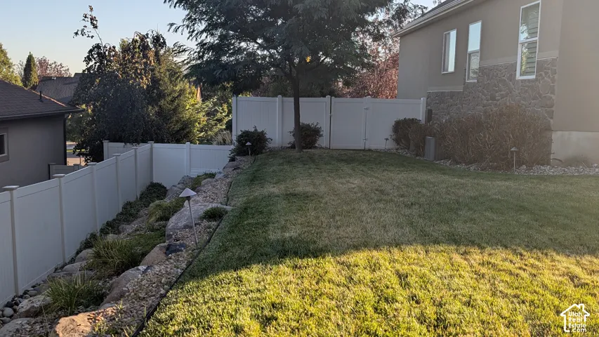 Expansive backyard featuring a manicured lawn, established landscaping, and a privacy fence