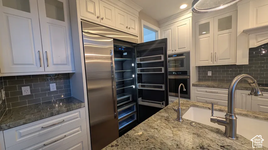 Gourmet kitchen featuring a built-in stainless steel refrigerator, double ovens, white shaker cabinetry, granite countertops, and a subway tile backsplash