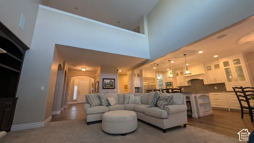 Open-concept living area with high ceilings, dark wood-finish built-in shelving, arched doorways, and a kitchen featuring white cabinetry and pendant lighting