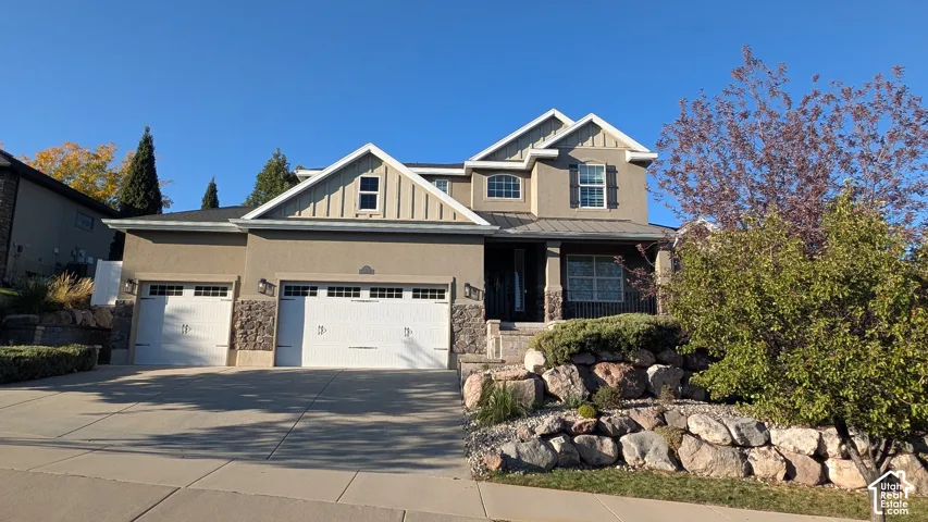 Stucco exterior with stone accents, two white garage doors, a covered porch, and a tiered rock landscaping