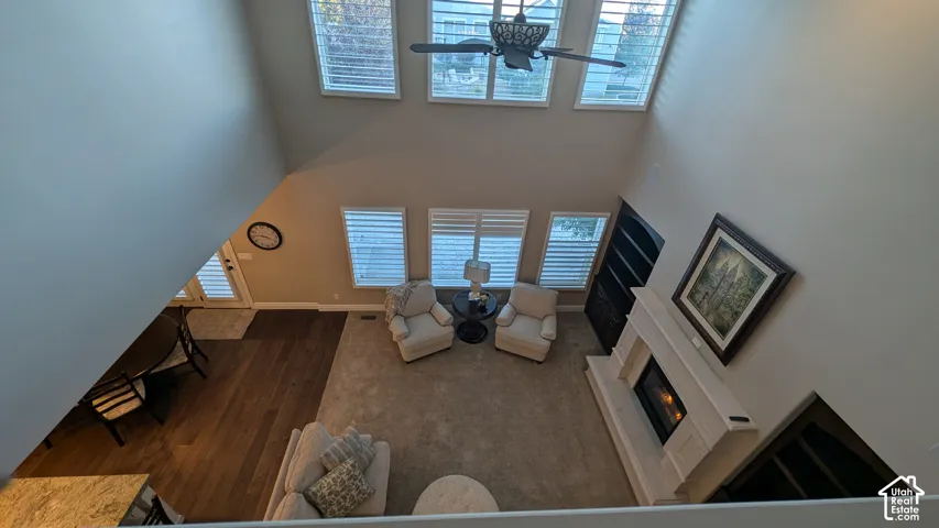 Two-story ceiling, multiple large windows, ceiling fan, fireplace with mantel, and wood-finish flooring