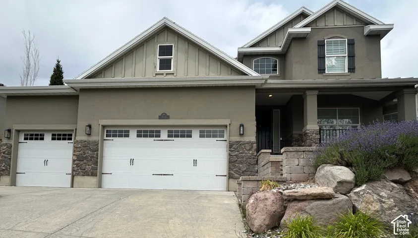 Stucco exterior with stone accents, covered front porch, and multi-pane garage doors
