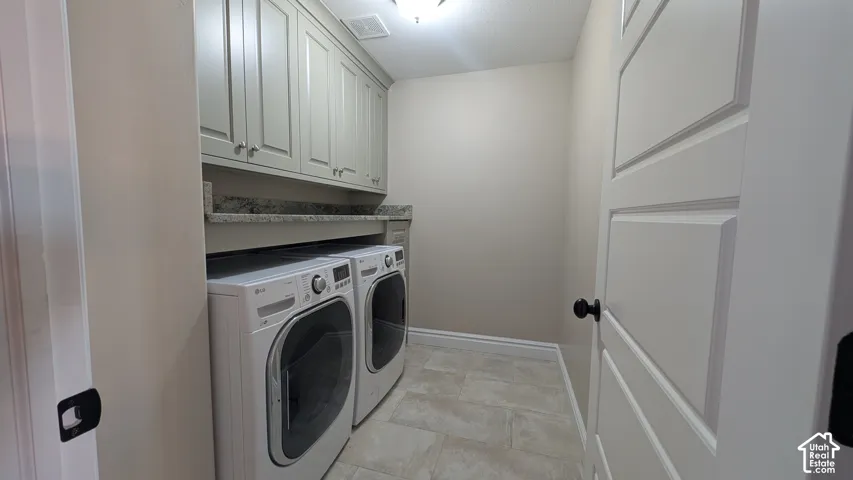 Functional laundry area featuring shaker-style cabinetry, a granite-finish countertop, and tile flooring