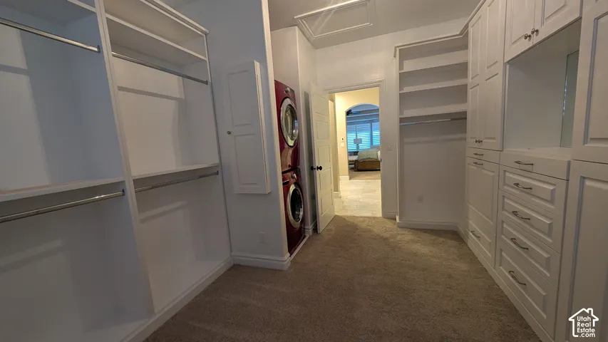 Master walk-in closet Custom built-in white cabinetry, built-in shelving, hanging rods, carpet flooring, and an arched doorway