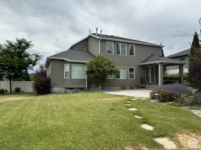 back side of home featuring Stucco exterior with multiple windows, covered patio, stone stepping path, and manicured lawn