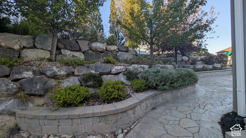 Tiered landscaping featuring natural stone retaining walls, block-built planters, mature trees, and established shrubbery