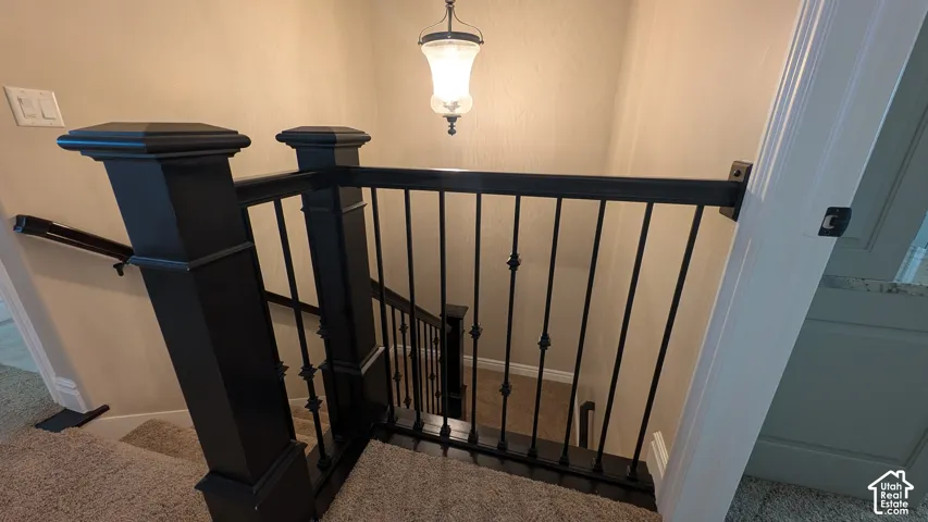 Staircase featuring dark wood newel posts, wrought iron balusters, and a clear glass pendant light fixture