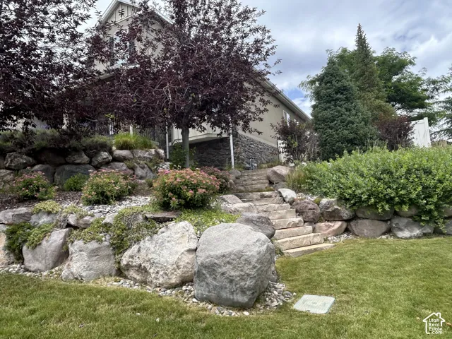 Manicured lawn with a terraced stone retaining wall, mature trees, and a stone staircase