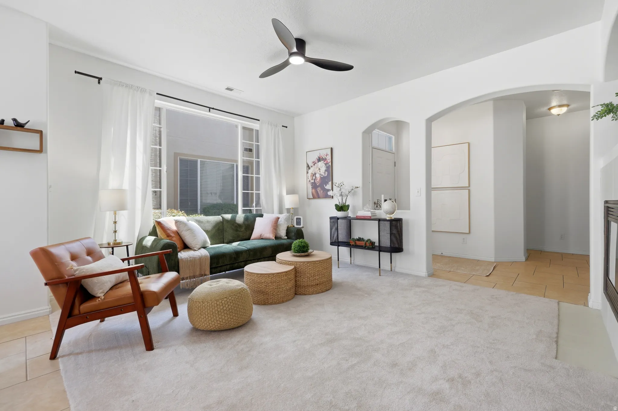 Spacious living area featuring a ceiling fan with integrated lighting, large sliding glass door, arched architectural details, and light-toned flooring