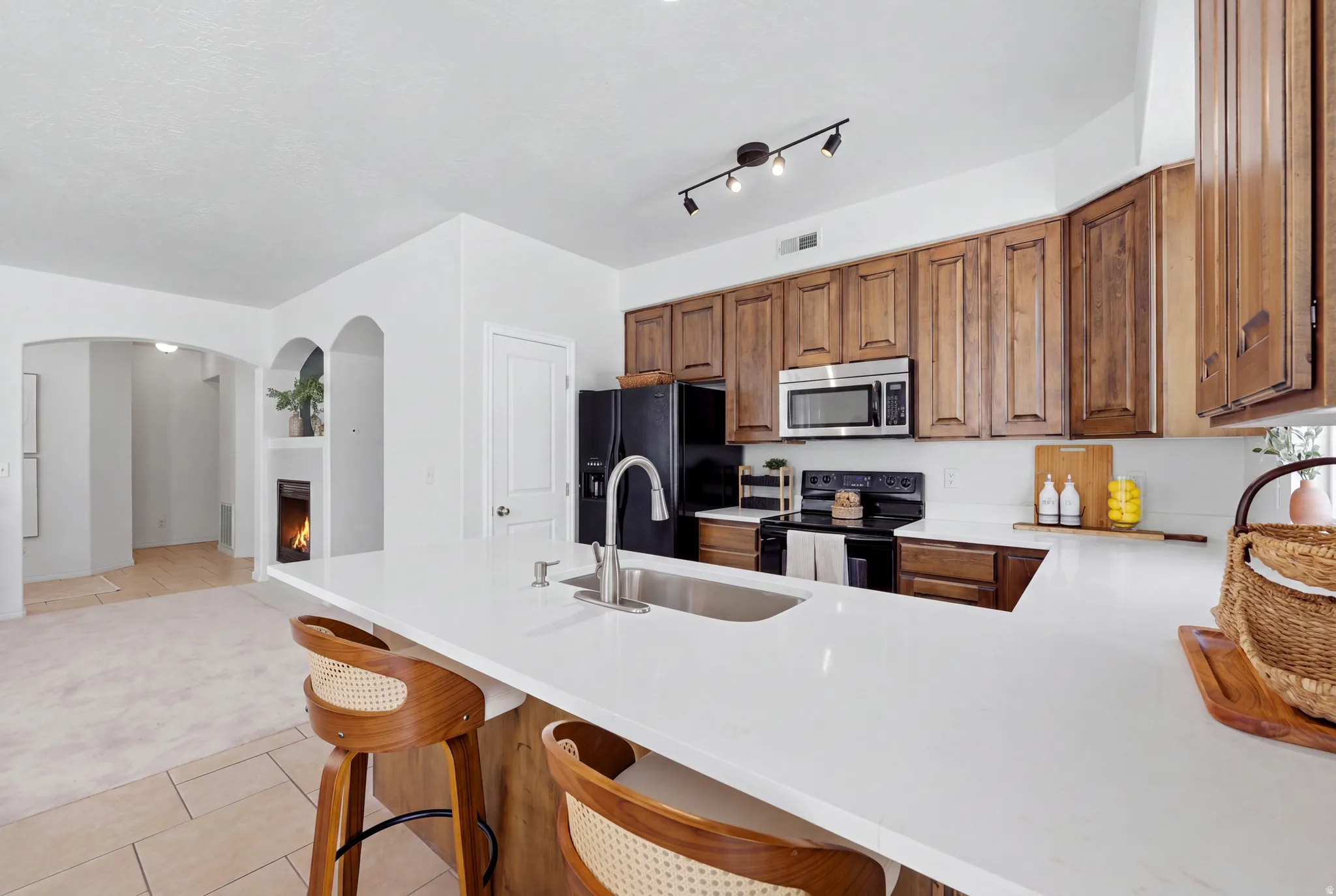 Kitchen featuring wood cabinetry, stainless steel microwave, black electric range, and a white countertop island with an integrated sink