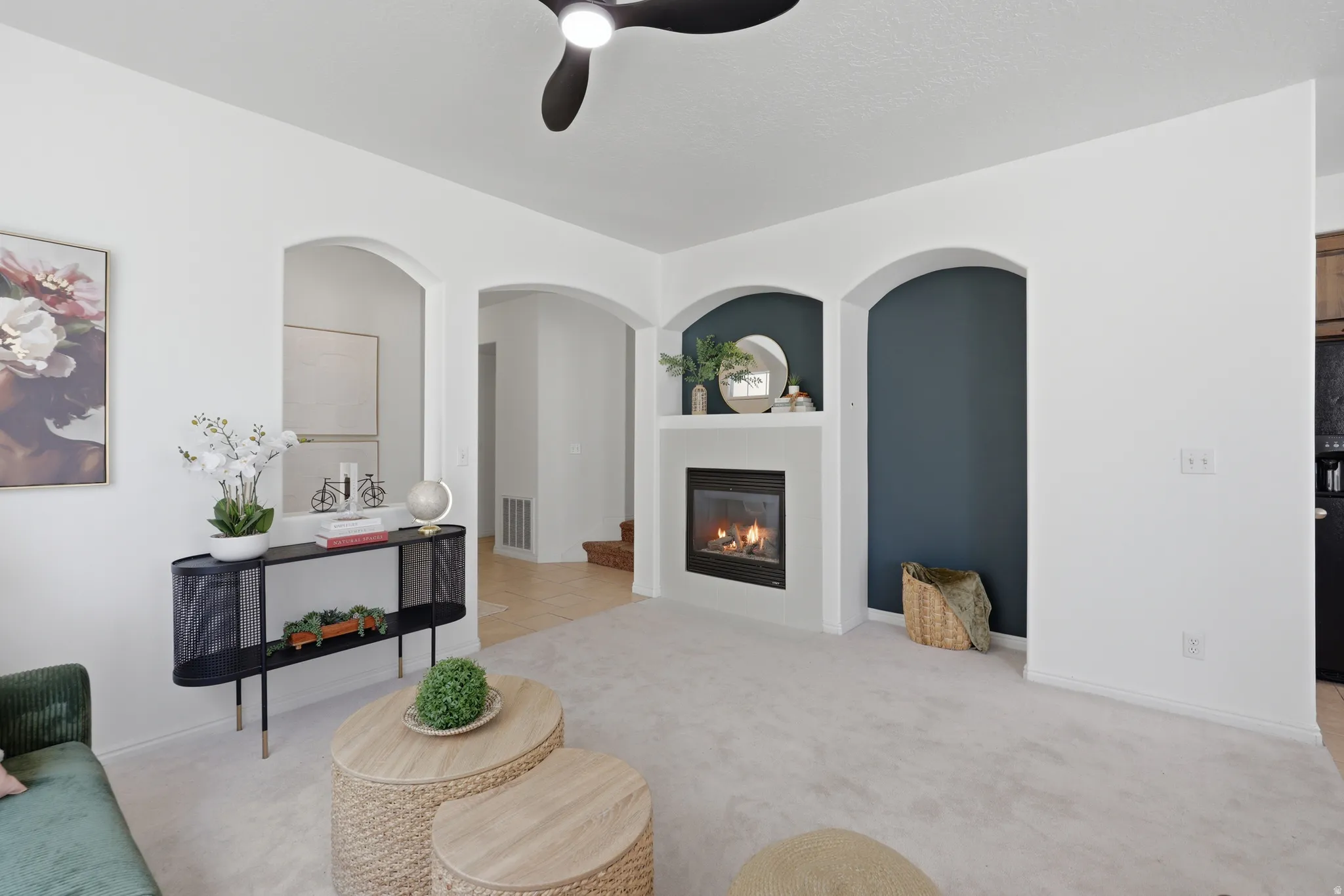 Archways leading to additional spaces, a built-in fireplace with a mantel, and a ceiling fan with integrated lighting