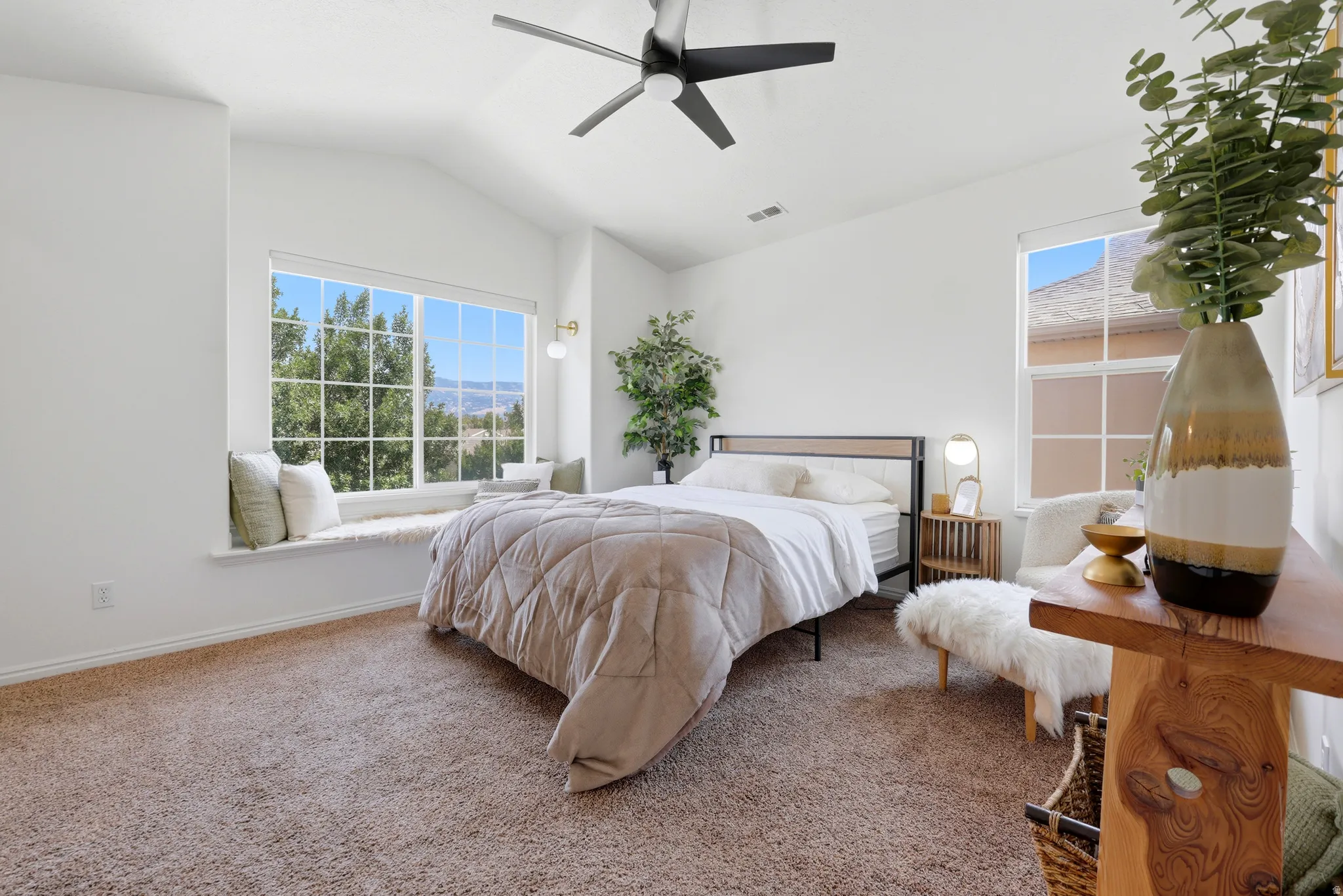 Vaulted ceiling, ceiling fan, carpet flooring, window seat, and large windows