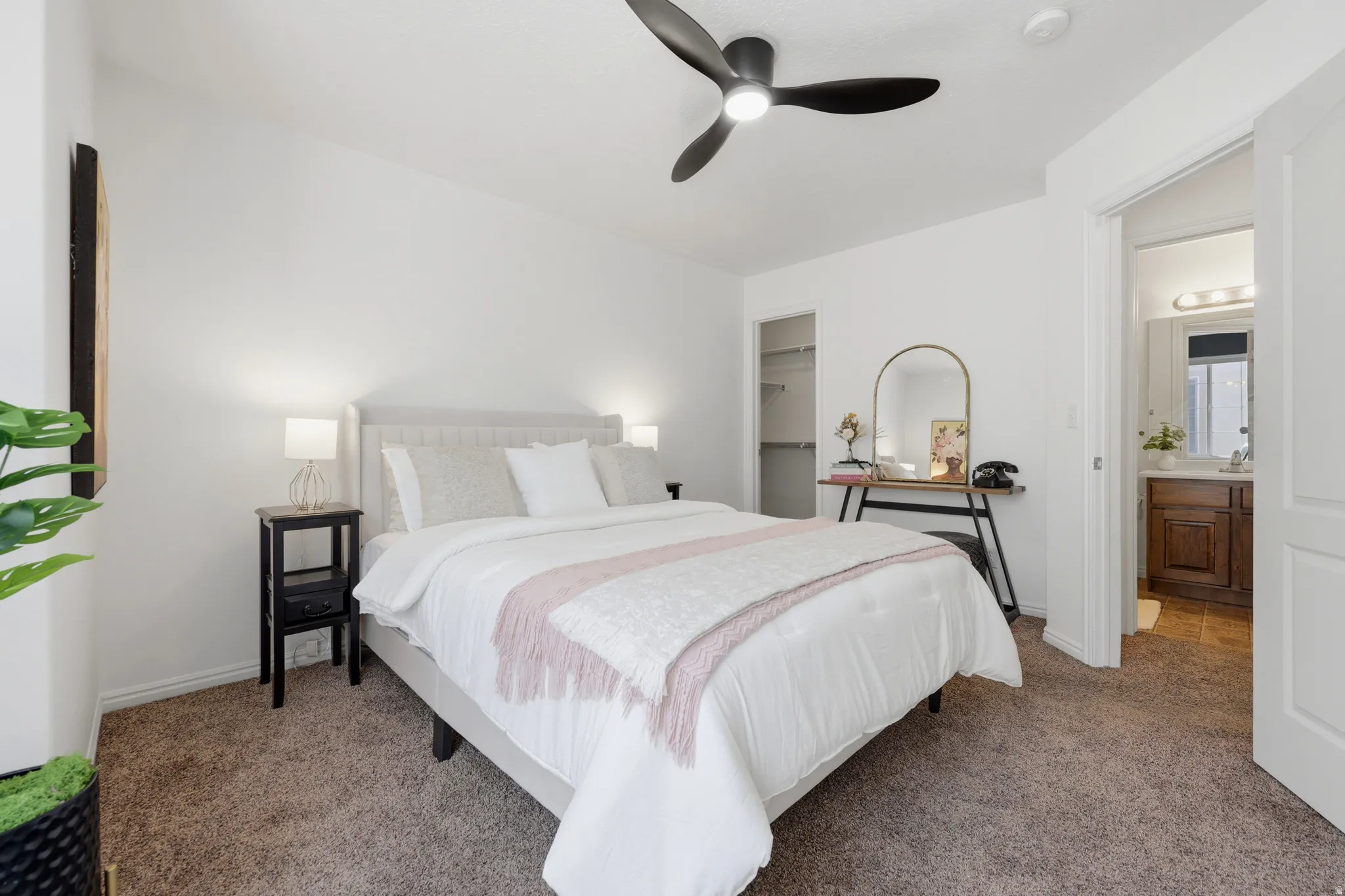 Primary bedroom featuring a vaulted ceiling with ceiling fan, carpeted flooring, dual nightstands with integrated lighting, and an ensuite bathroom with vanity and mirror visible through the adjacent doorway