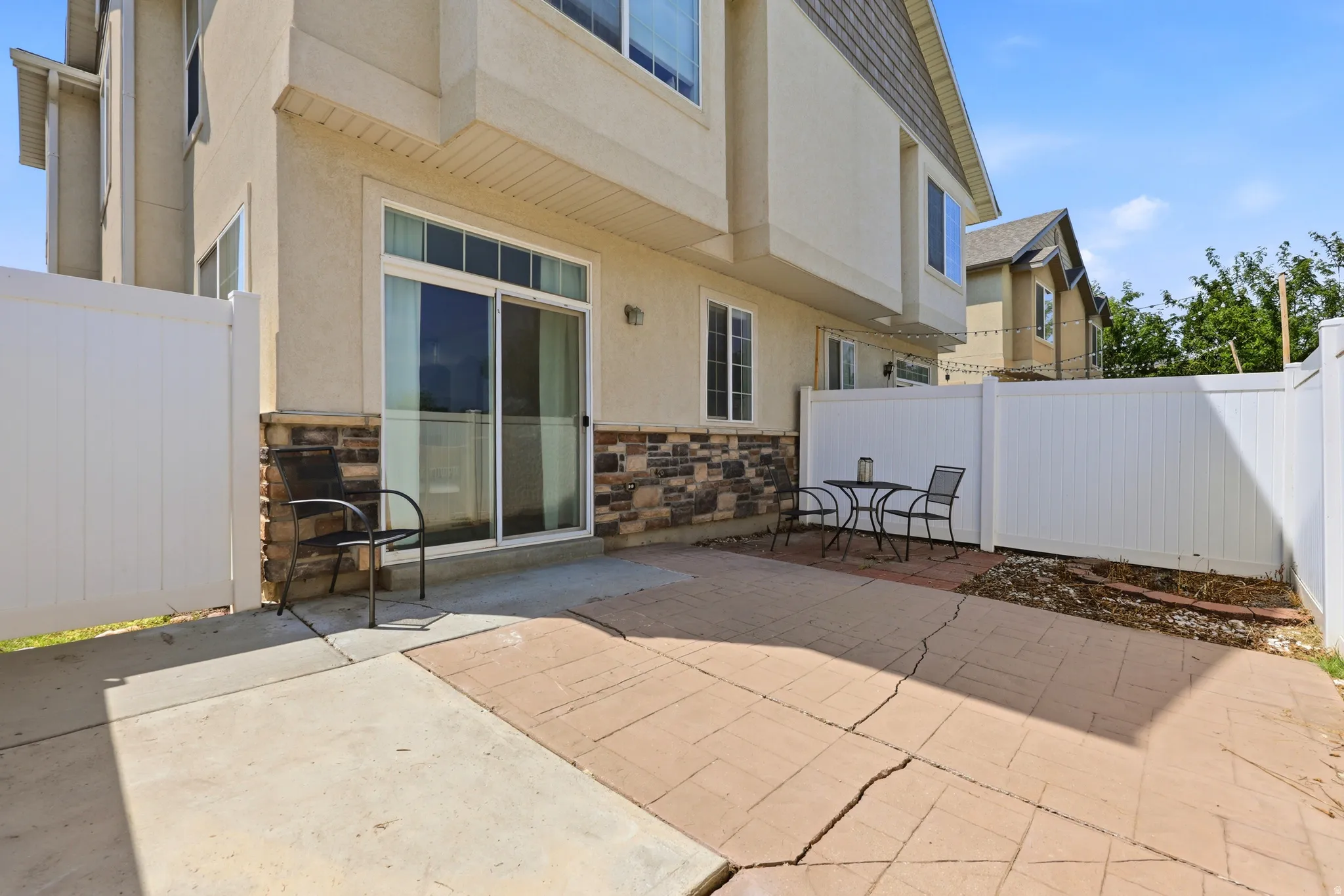 Private patio space featuring a sliding glass door, white privacy fencing, and a stone veneer foundation