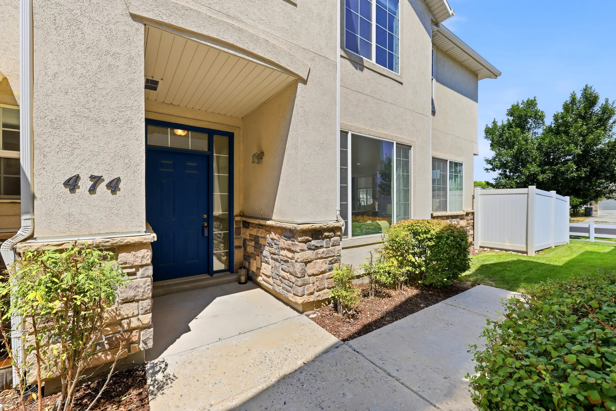 Stucco exterior with stone veneer accents, a prominent blue entry door, an overhead awning, and mature landscaping