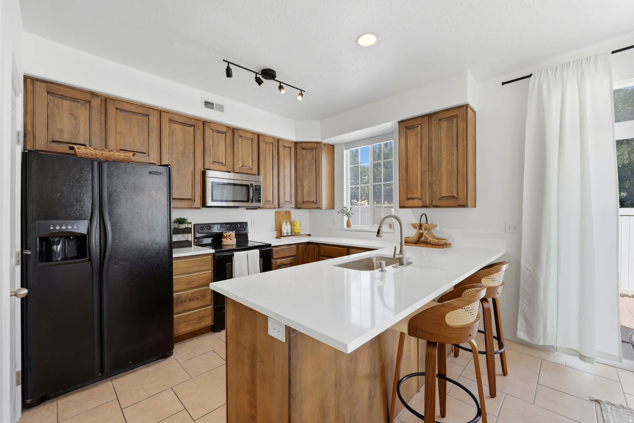 Kitchen featuring wood cabinetry, white countertops, stainless steel microwave, black appliances, and tiled flooring