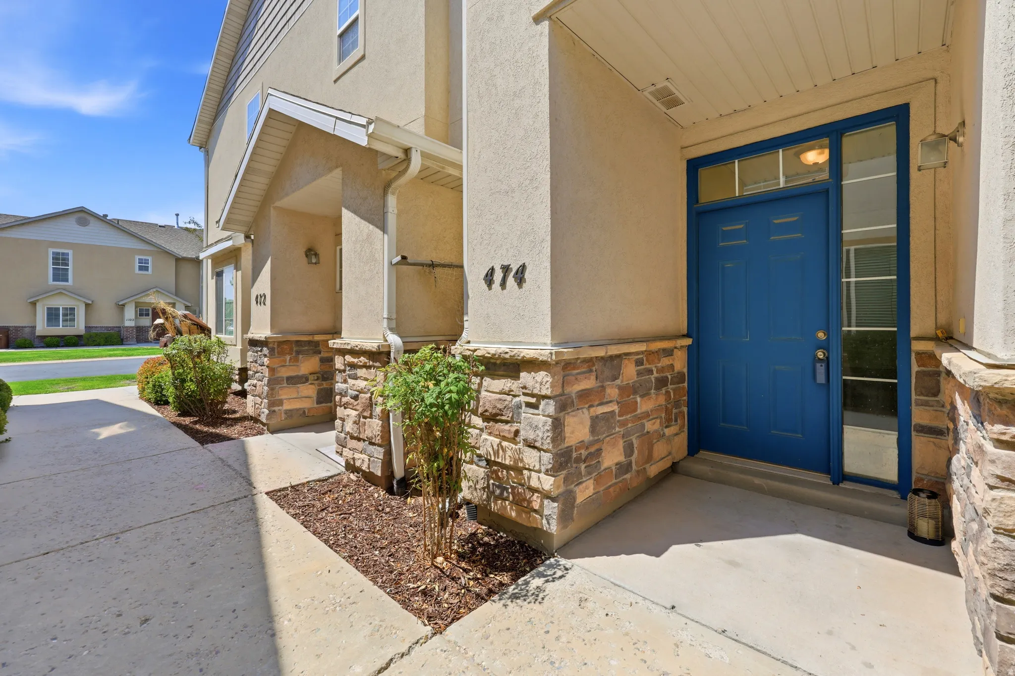 Stucco exterior with stone veneer accents, blue paneled entry door with transom window, and concrete walkway